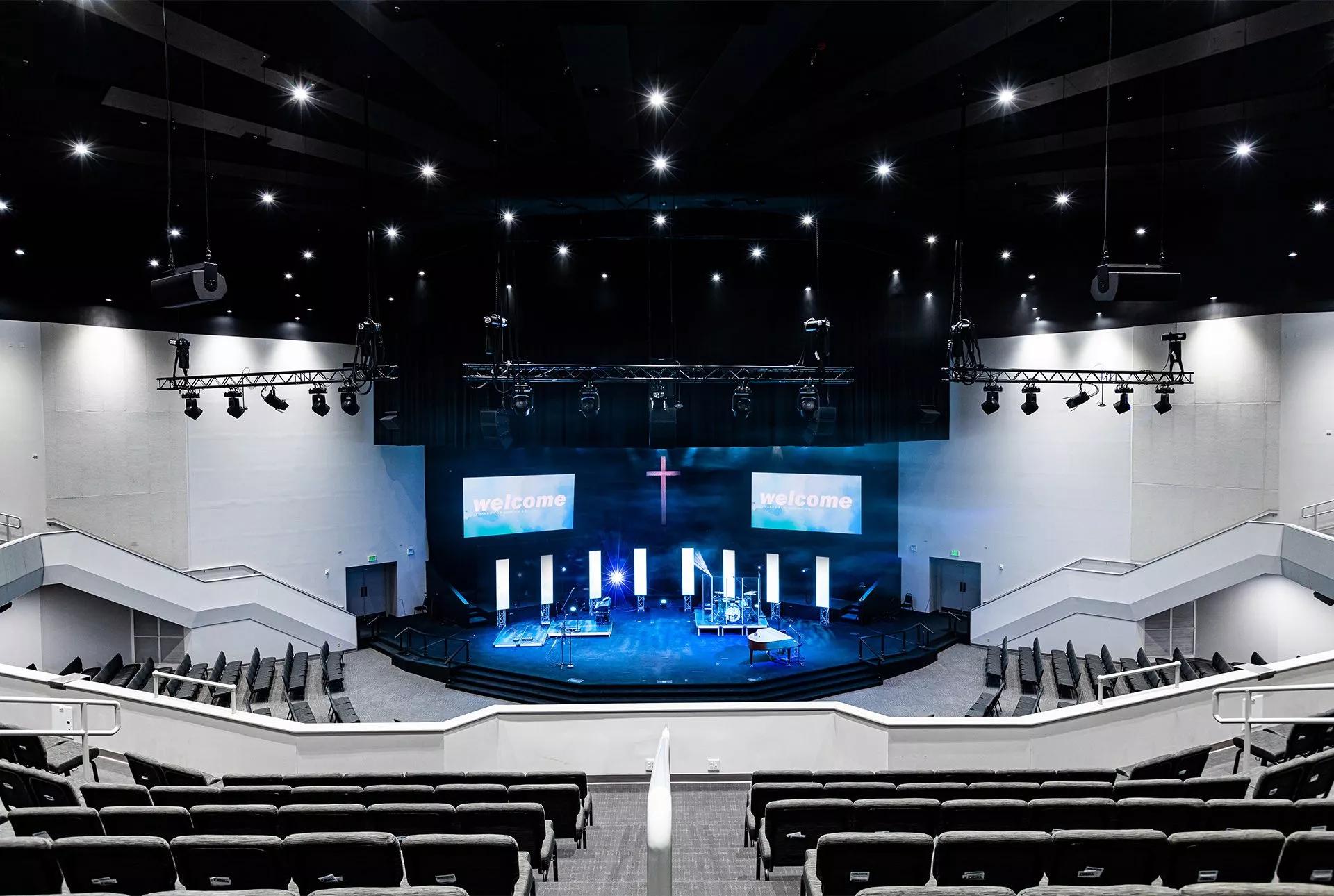 Speakers hang from the ceiling of a large church worship space.