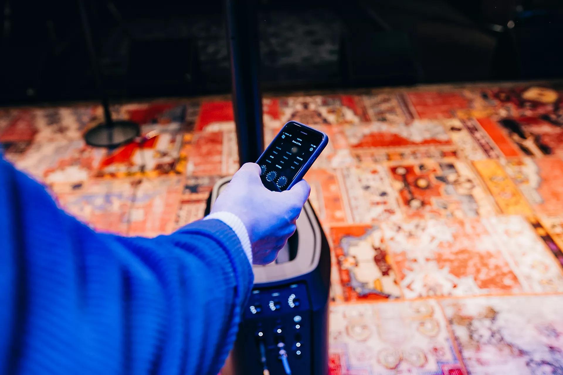 A hand using a mobile device connected to a Bose L1 Pro Line Array system
