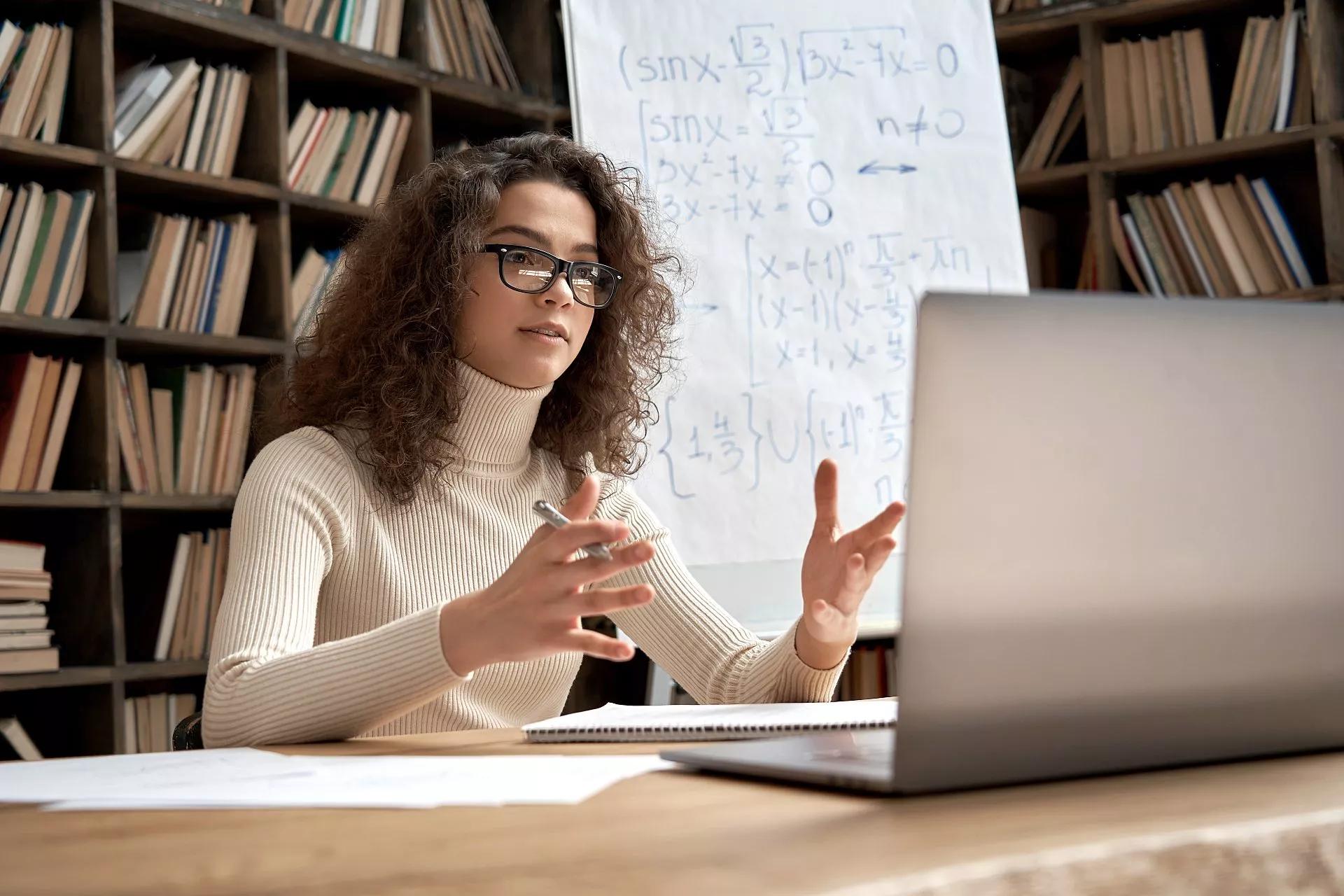 A teacher sits in front of a laptop and leads a class using videoconferencing.