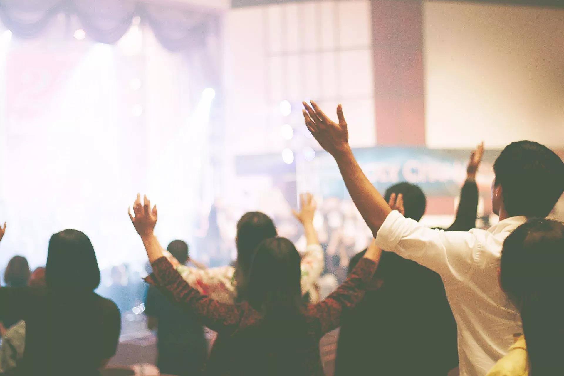 Worshippers stand facing the front of a church with their hands in the air.