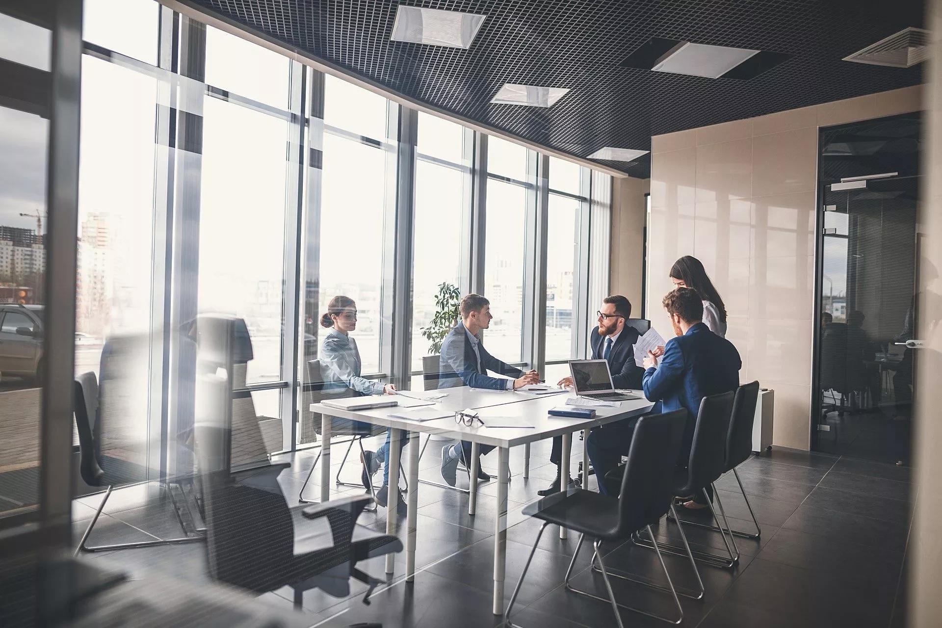 A team of five colleagues meets in a sophisticated, well-lit conference room with glass walls.