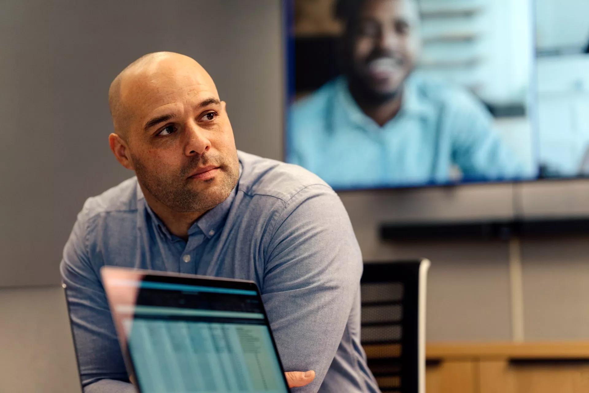 A businessman sitting in front of a video screen with three remote colleagues