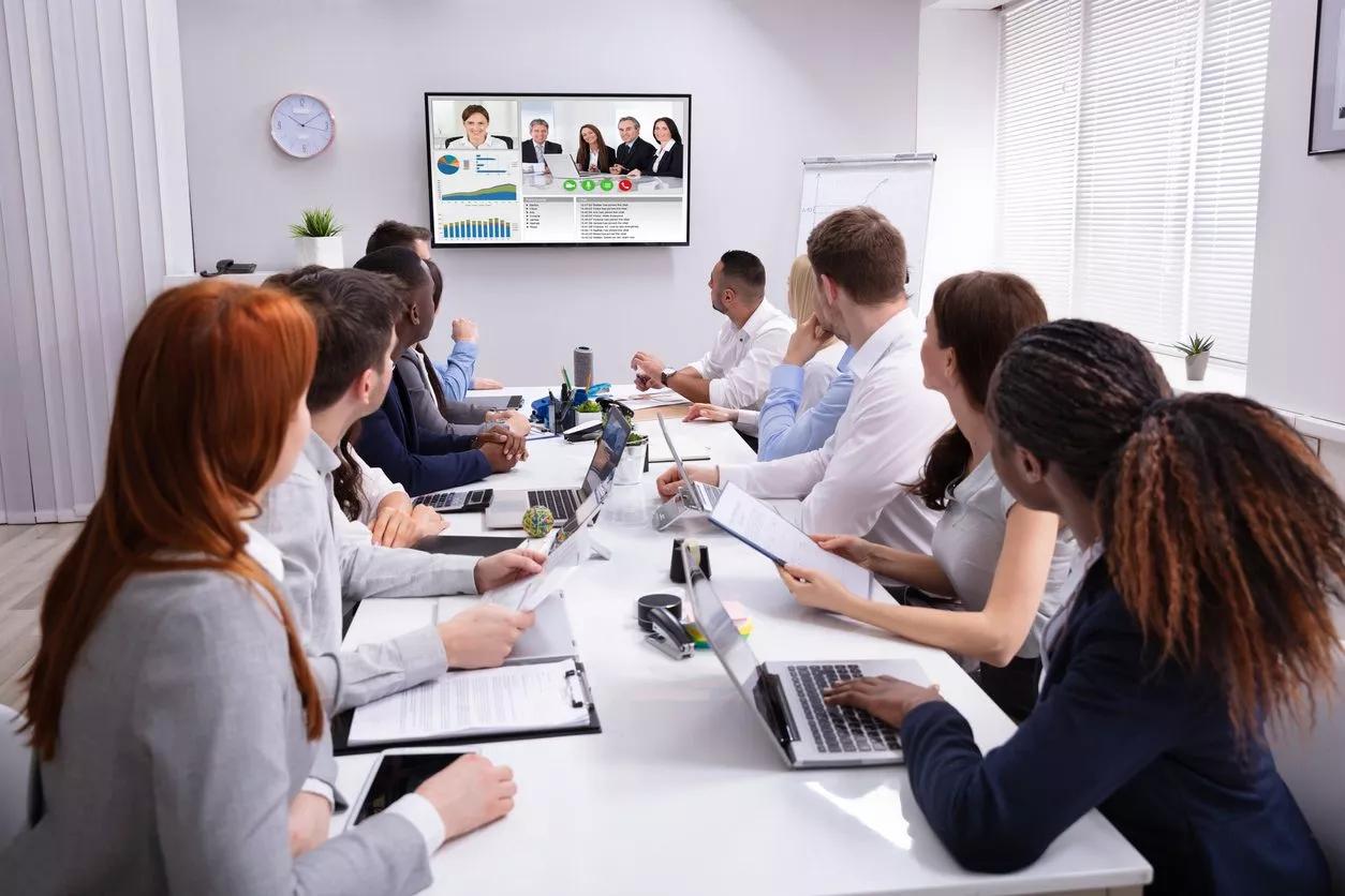 Office workers participate in a videoconferencing session with some at a long meeting table.