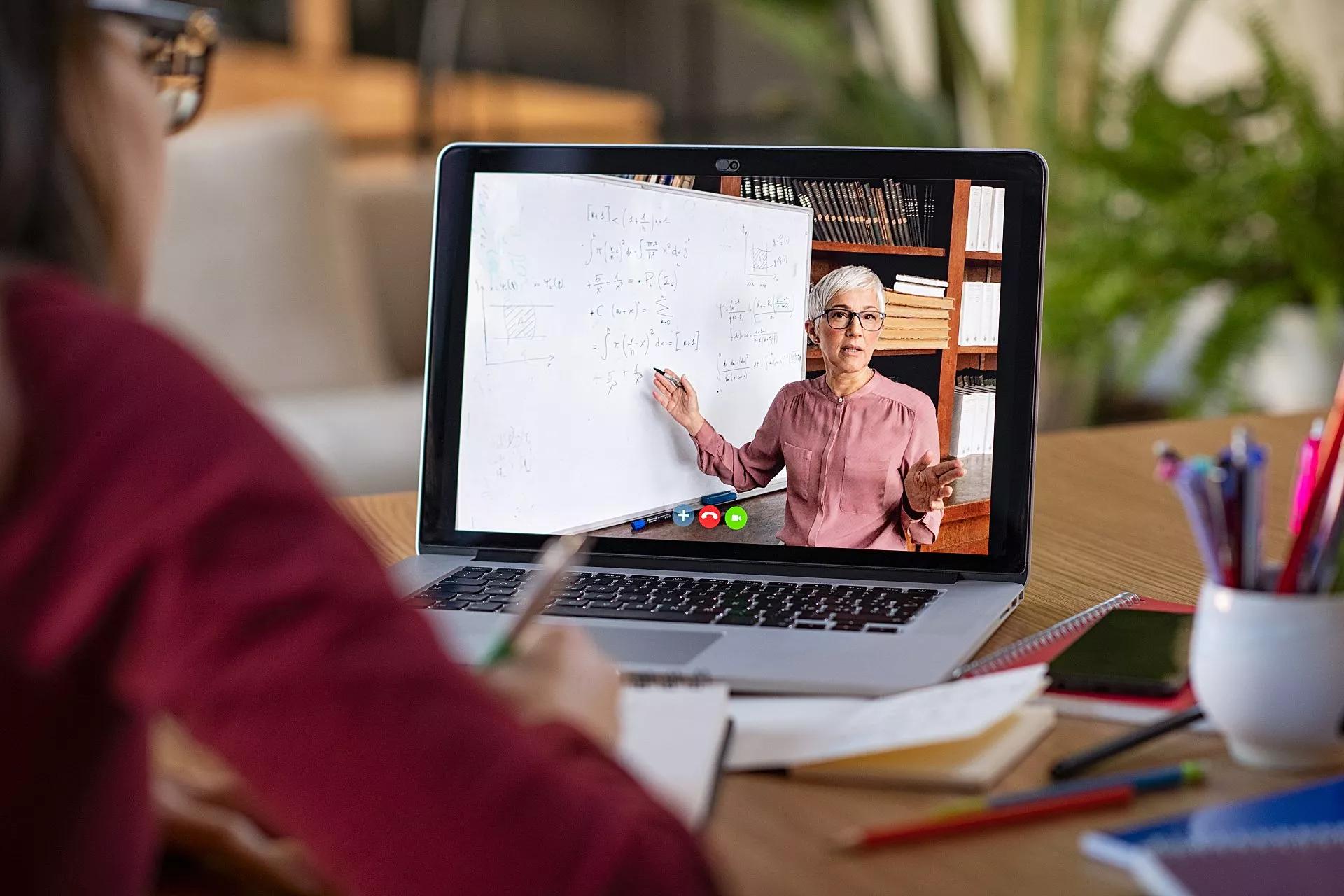 A participant takes notes on a notepad while watching a webinar on a laptop