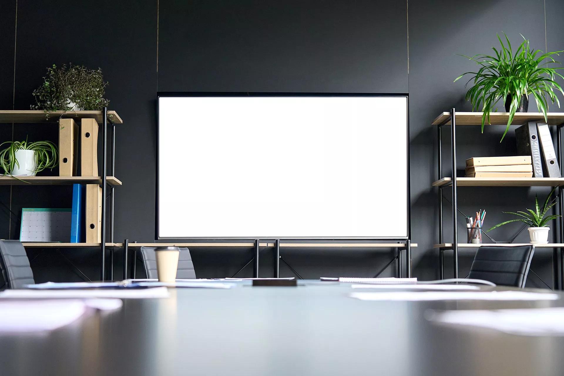 A blank video screen in front of a large conference table.