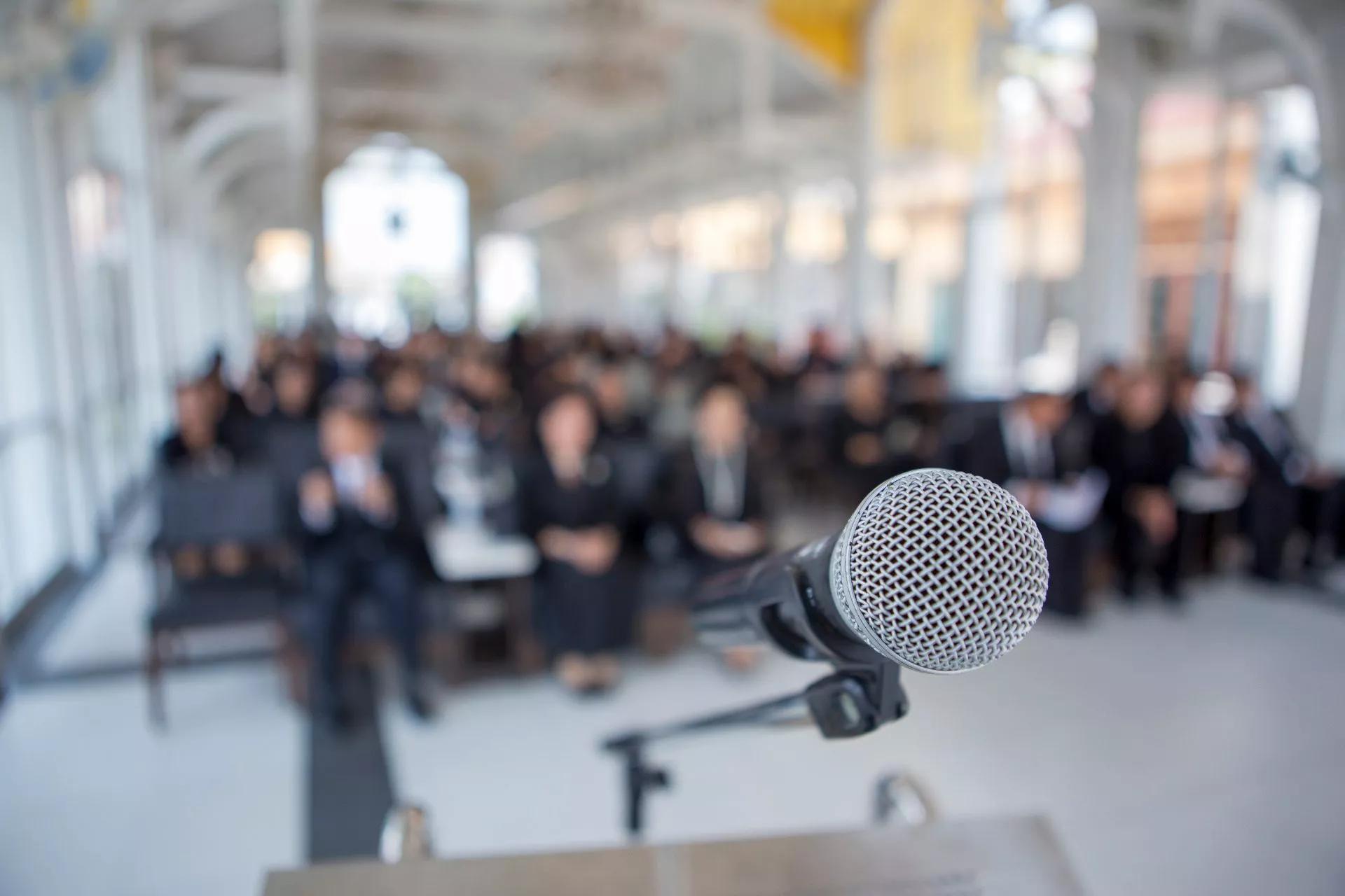 Church attendee with hand lifted in front of a person on stage speaking into a microphone