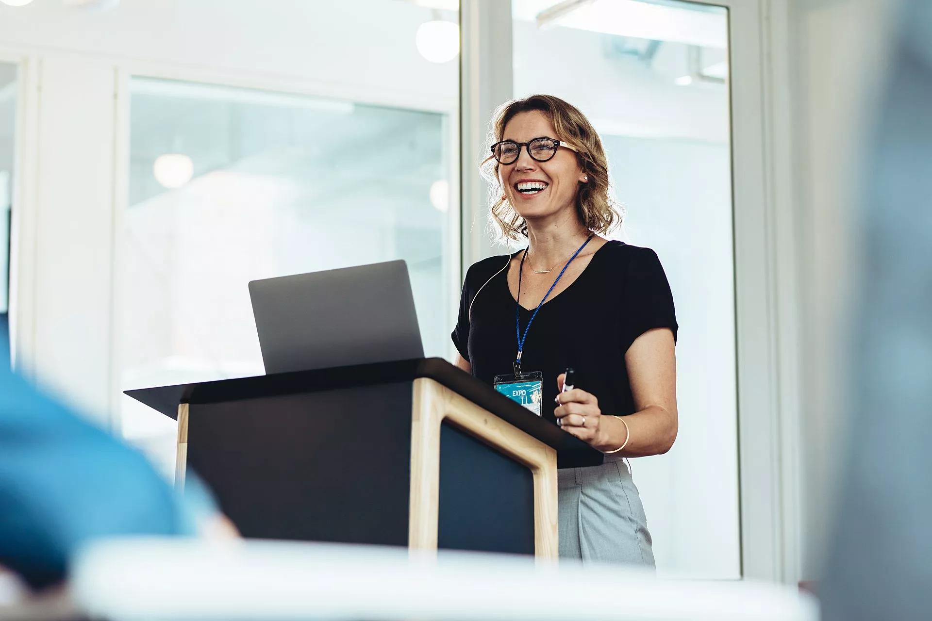 Woman standing at a lectern with her laptop gives a presentation to conference attendees