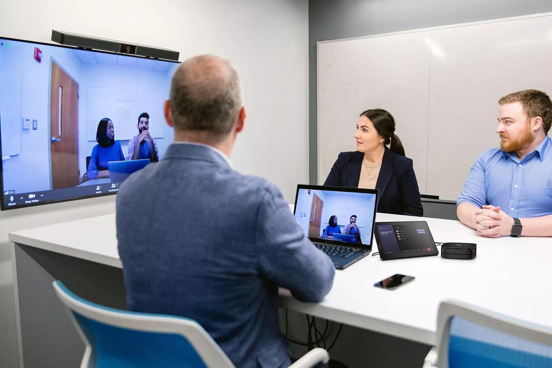 Empleados sentados en una mesa de conferencias mientras utilizan la solución de audio para techo ES1 de Bose Professional.